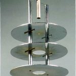 LUSTRE, René Herbst,  Important lustre moderniste en bronze repris autour, composé de deux tiges verticales et de trois disques d’acier. Eclairage par deux ampoules dépolies enchâssées dans les disques Modèle de 1929. Présenté au Salon d’Automne de 1931 à Paris. Hauteur 63 cm – Diamètre : 35 cm